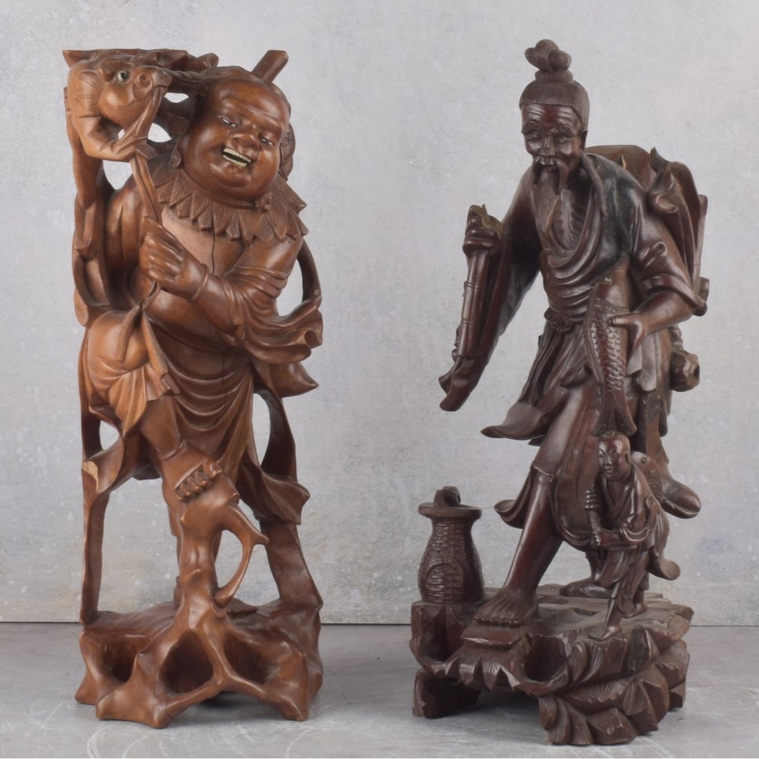 Antique Carved Chinese Wood Sculptures: Two (2) Antique Carved Organic Material Chinese Wood Sculptures. One (1) fisherman with child, basket and fish, measures: 17" high, 7" wide, 7" deep, one (1) man playing with a food dog, 17" high, 6-1