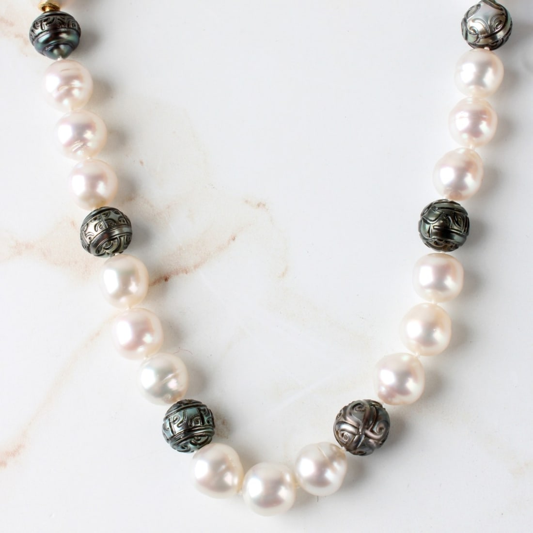 South Sea Pearl Necklace: Single Strand 13.1-10.2 South Sea White and Finely Etched Black Pearl Necklace with 18 Karat Yellow Gold Clasp. Pearls with good luster and polish with minor natural blemishes. Clasp stamped 18K 750.