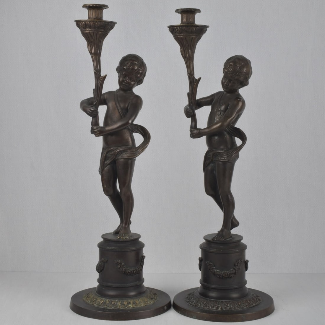 Pair of Bronze Figural Candlesticks: Pair of Bronze Vintage Figural Candlesticks in the Form of Standing Cherubs. Measures: 23-1/4" high, bases: 8-1/4" diameter. Kodner Galleries offers phone and absentee bidding at a low, flat 21%