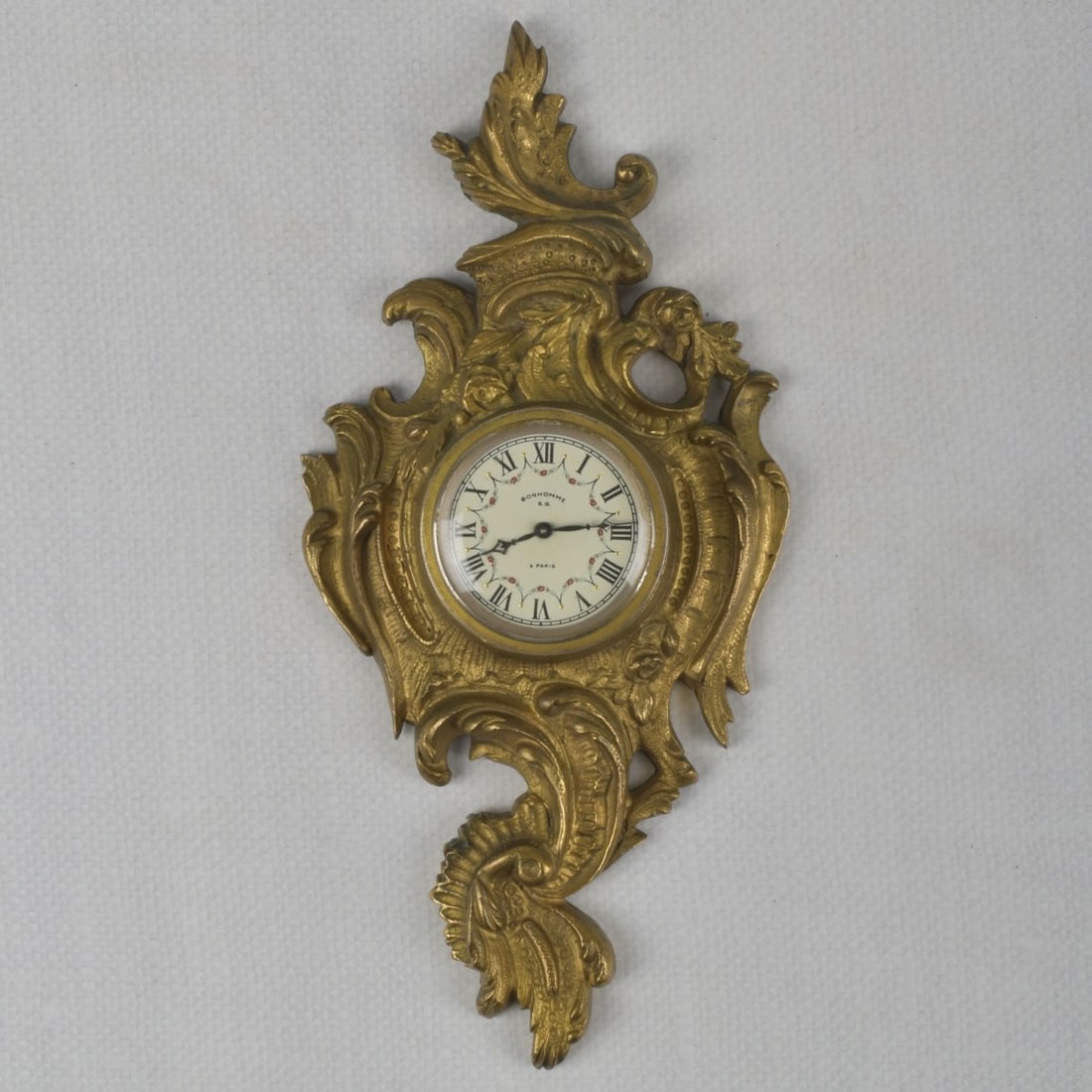 French Bayard Gilt Bronze Clock: French Bayard Gilt Bronze Rococo Wall Clock Retailed by Bonhomme Paris with a White Face Dial with Black Enameled Arabic Numerals. Face measures: 1-7/8" diameter, clock overall measures: 10-1/2"