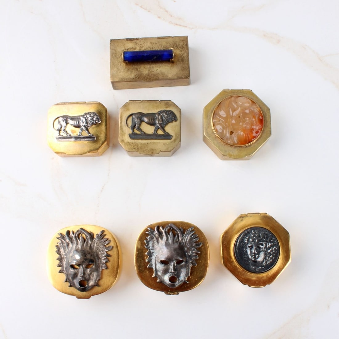 Gilt Metal Pill Boxes: Collection of Seven Vintage Hinged Gilt Metal Pill Boxes with Tops Accented with Silver Masks, Lions or Hardstones. Signed Jared. Largest boxes measure 1-3/8" square. Kodner Galleries offers phone