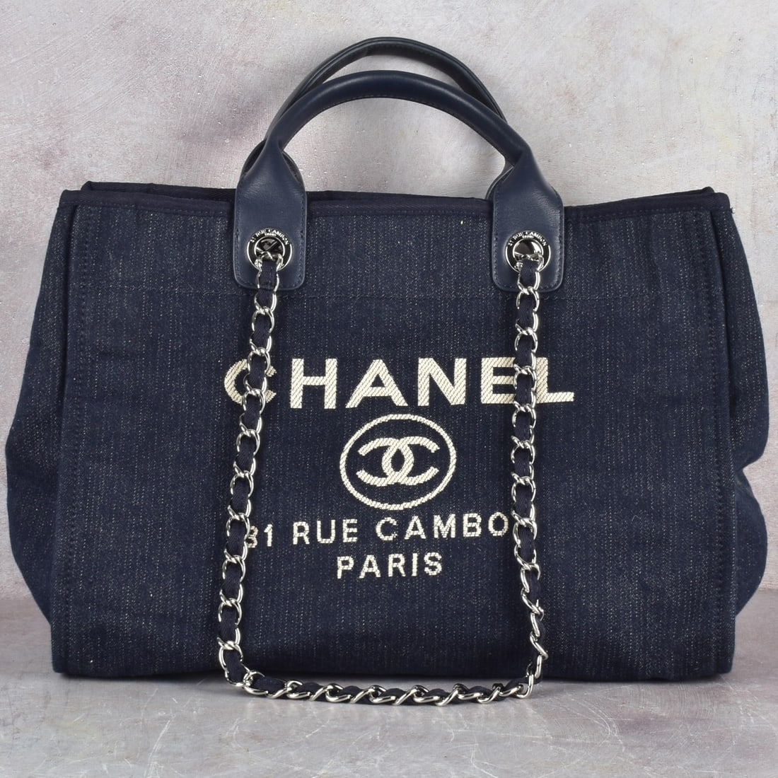 Replica Chanel Deauville Tote: Replica Chanel Deauville Navy Blue Denim Tote Bag with Silver Hardware. Having two Navy blue leather handles, two woven chain and interwoven cloth shoulder straps, and silk screened logo type and an o
