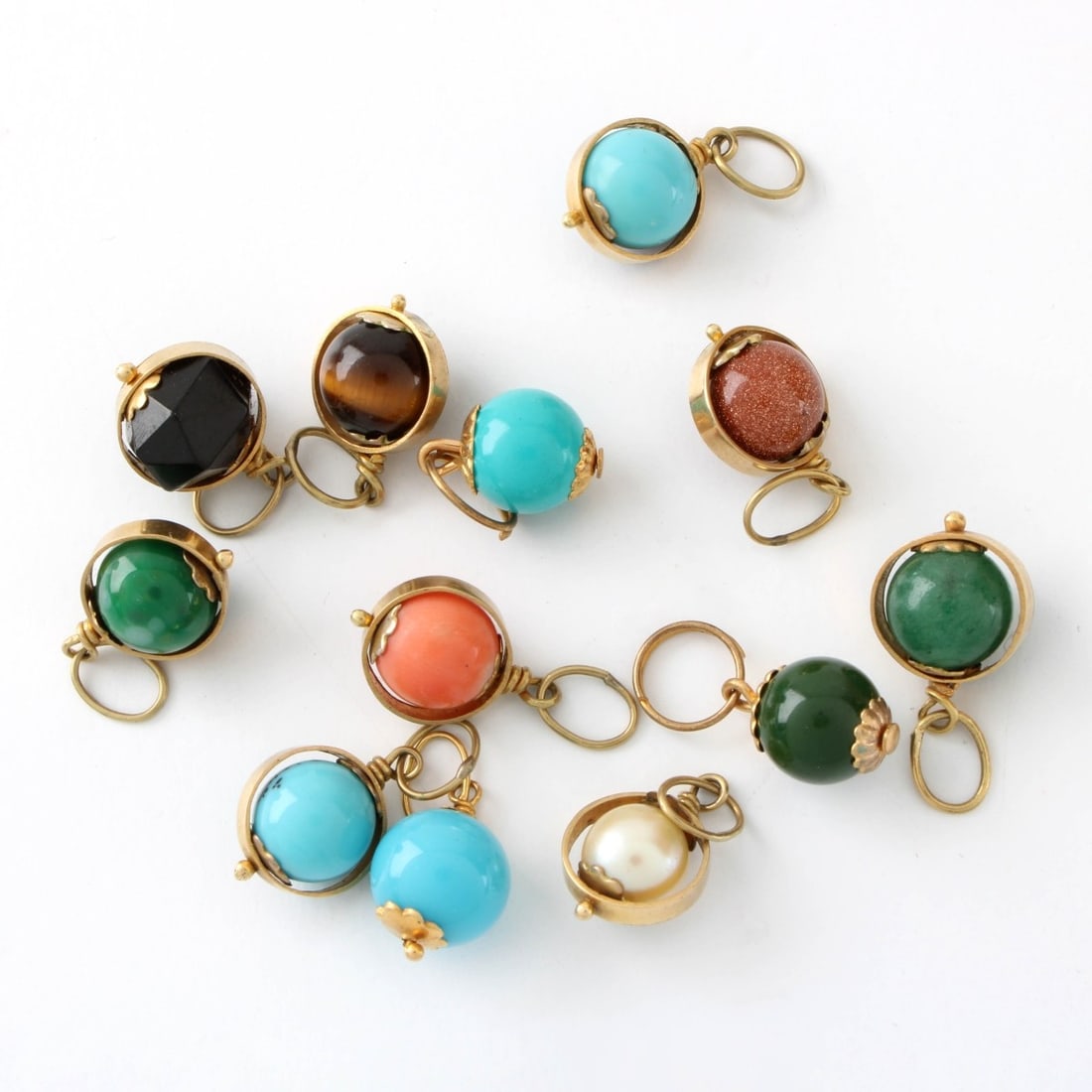 14K and Hardstone Pendants: Twelve (12) Vintage 14 Karat Yellow Gold and Hardstone Pendants. Variously set with coral, turquoise, black onyx, tiger eye and more. Each measures 1-4" W, 5/8" L. Approx. total weight: 14.15 grams.
