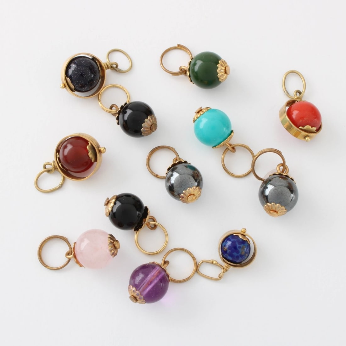 14K and Hardstone Pendants: Twelve (12) Vintage 14 Karat Yellow Gold and Hardstone Pendants. Variously set with coral, turquoise, black onyx, amethyst and more. Each measures 1-4" W, 5/8" L. Approx. total weight: 12.98 grams.