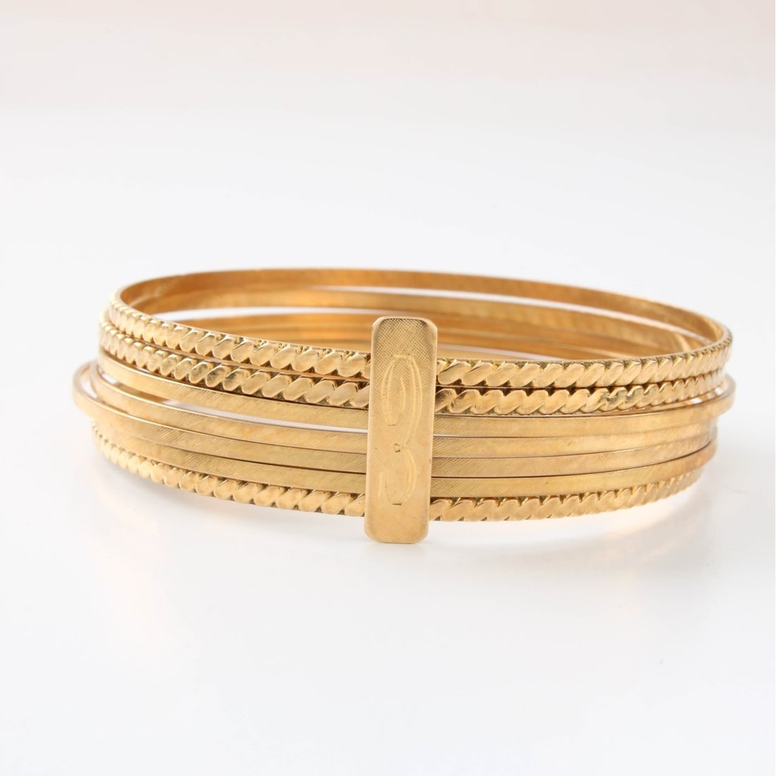 18K Stacked Bangle Bracelets: Vintage Set of Seven (7) Stacked Bangle Bracelets with Retro Design and with Yellow Gold Clasp. Measure 2-1/2" diam. Approx. total weight: 22.16 grams. Kodner Galleries offers phone and absentee