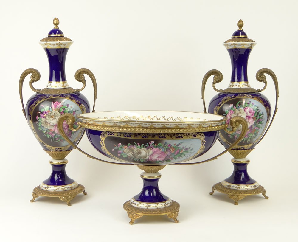 20th Century Three (3) Piece Sevres-style Gilt Bronze: 20th Century Three (3) Piece Sevres-style Gilt Bronze Mounted Cobalt Porcelain Garniture Set with Painted Floral Reserves Comprising a Pair of Urns and a Footed Compote. Illegible Artist Signature to