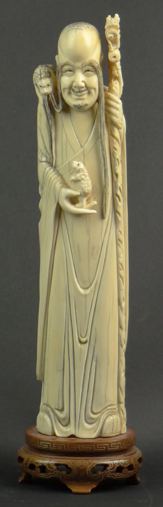18/19th Century Chinese Carved Ivory Figure of a Man: 18/19th Century Chinese Carved Ivory Figure of a Man with Very Long Eyebrows Carrying a Staff with the Head of a Dragon, Holding a Frog with a Buddhist Lion Perched on his Shoulder. Pinned to Wooden B