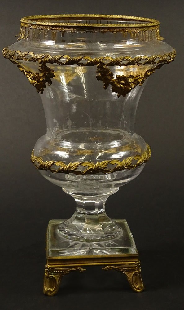19/20th Century Louis XVI style Gilt Bronze Mounted Cut: 19/20th Century Louis XVI style Gilt Bronze Mounted Cut Crystal Urn. Unsigned. Losses to Bronze, Scratches/Chips to Crystal, Antique Condition. Measures 11-5/8 Inches tall and 7 Inches Wide. Shipping 