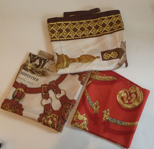 Three Elegant Hermes Scarves: 1.) The red/gold scarf measures 35" x 35" and is titled Les Cavaliers D' OR Rybal 100% SOIE. 2.) The gold/white/brown scarf measures 35" x 35" Signed "Cuiveeries Hermes Paris F. De La Perriere" 3.) Th