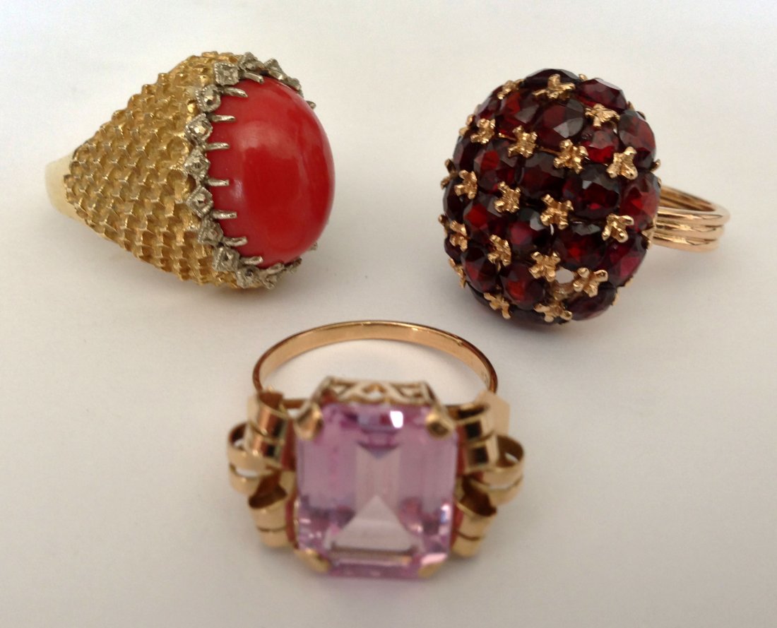 3 18K Gold Rings Cocktail Rings: 3 signed 18K gold rings. One with 27 rubies (Size 7), one with cabochon coral (size 6.5) and one with a pink colored stone ( Size 7). Gross weight is 18.1 dwt.