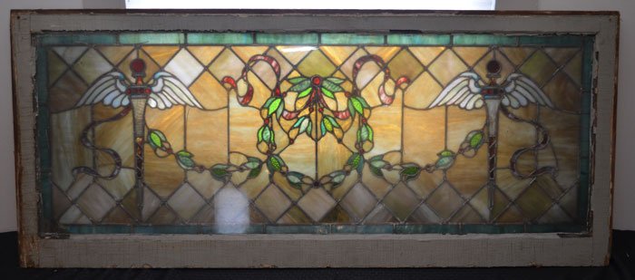 Large Antique Stained Glass Window: Stunning stained & leaded glass window featuring a laurel wreath and swag with winged scepter. Frame: 56" x 24" glass sight: 52" x 19"