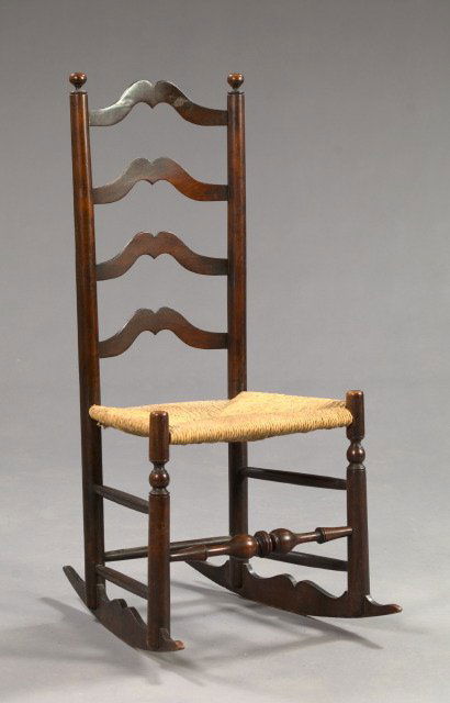 American Cherrywood Rocking Chair: Early American Stained Cherrywood Ladderback Carpet-Cutter Rocking Chair, early 19th century, the back with four shaped and curved slats, the seat woven in rush and the front legs joined by a bulbous