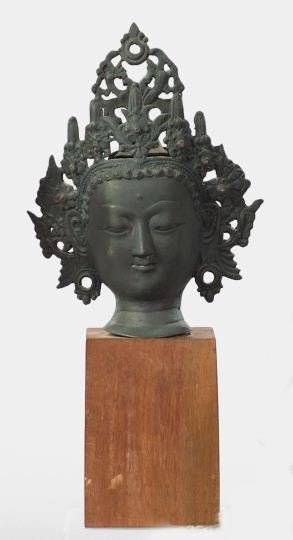 Nepalese Patinated Bronze Head: Nepalese Patinated Bronze Head of the Elaborately Crowned Youthful Buddha, third quarter 19th century, the crown set with seven small coral cabochons, presented on a square walnut pedestal base, h. 14