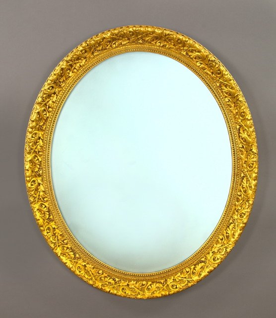 Large Carved Giltwood and Plaster Mirror: Large Carved Giltwood and Plaster Oval Looking Glass, in the Napoleon III style, the deep giltwood frame with a bas-relief rinceau of tangent foliate scrolls, h. 41-1/2", w. 36".