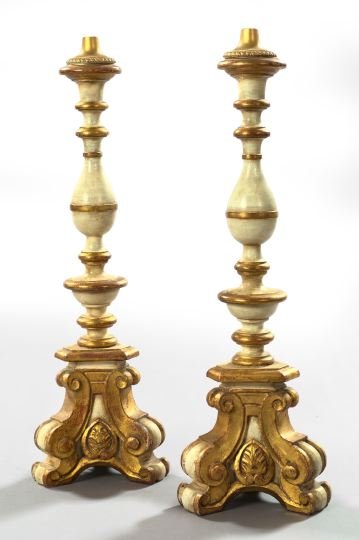 Italian Giltwood Altar Sticks Lamps: Imposing Pair of Italian White-Painted and Giltwood Altar Sticks, first quarter 20th century, the turned and carved tripodal sticks now mounted as table lamps, the brass harps fitted with tall oviform