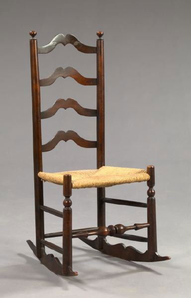 American Cherrywood Ladderback Rocking Chair: Early American Stained Cherrywood Ladderback Carpet-Cutter Rocking Chair, early 19th century, the back with four shaped and curved slats, the seat woven in rush and the front legs joined by a bulbous
