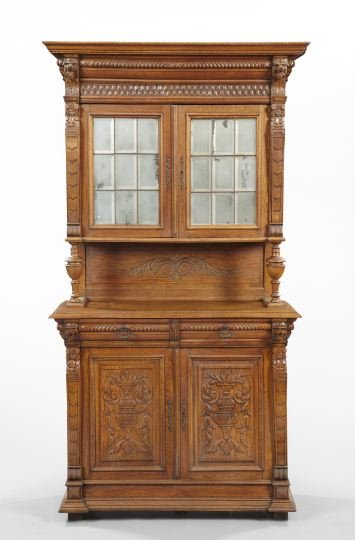 Continental Oak Cupboard,: Continental Oak Cupboard, ca. 1900, in two parts, the upper section with a projecting molded cornice over a carved frieze, each end mounted with a leonine masque, the pair of doors with leaded glass m