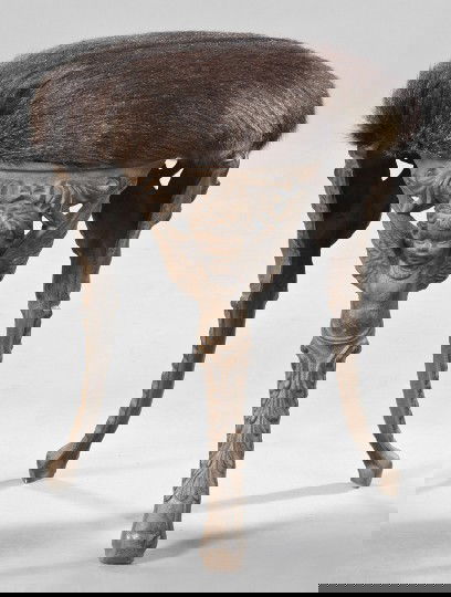 Belle Epoque Cast-Iron Tripodal Stool: Belle Epoque Cast-Iron "Winged Putto Masque" Tripodal Stool, first quarter 20th century, the circular seat presently upholstered in deep reddish-brown cowhide, h. 17-1/2", dia. 14".