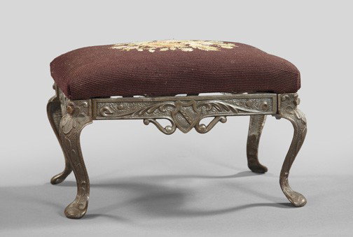 Continental Silvered Cast-Iron Footstool: Continental Silvered Cast-Iron Cabriole-Legged Footstool, first quarter 20th century, in the Baronial taste, each seat rail centered with a bas-relief heraldic shield, the padded seat upholstered in s
