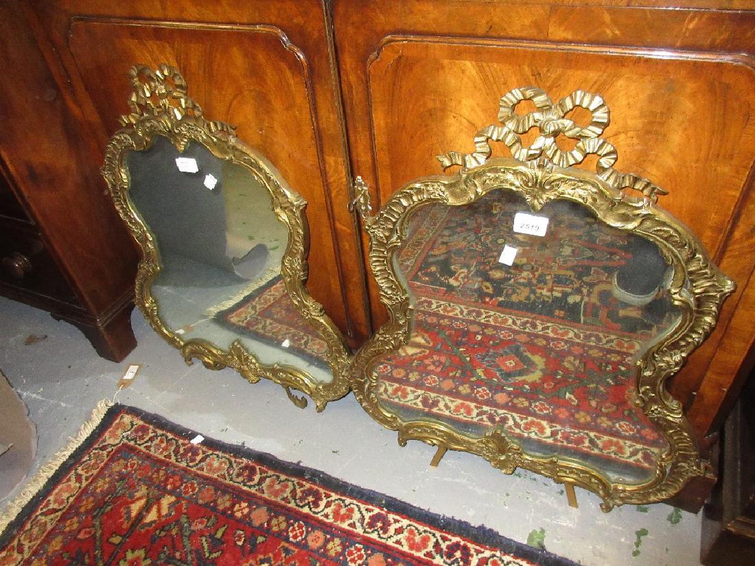 Pair of late 19th or early 20th Century gilt brass: Pair of late 19th or early 20th Century gilt brass cartouche shaped table mirrors with relief decorated shaped frames and bow surmounts with original back stands, 26ins high
