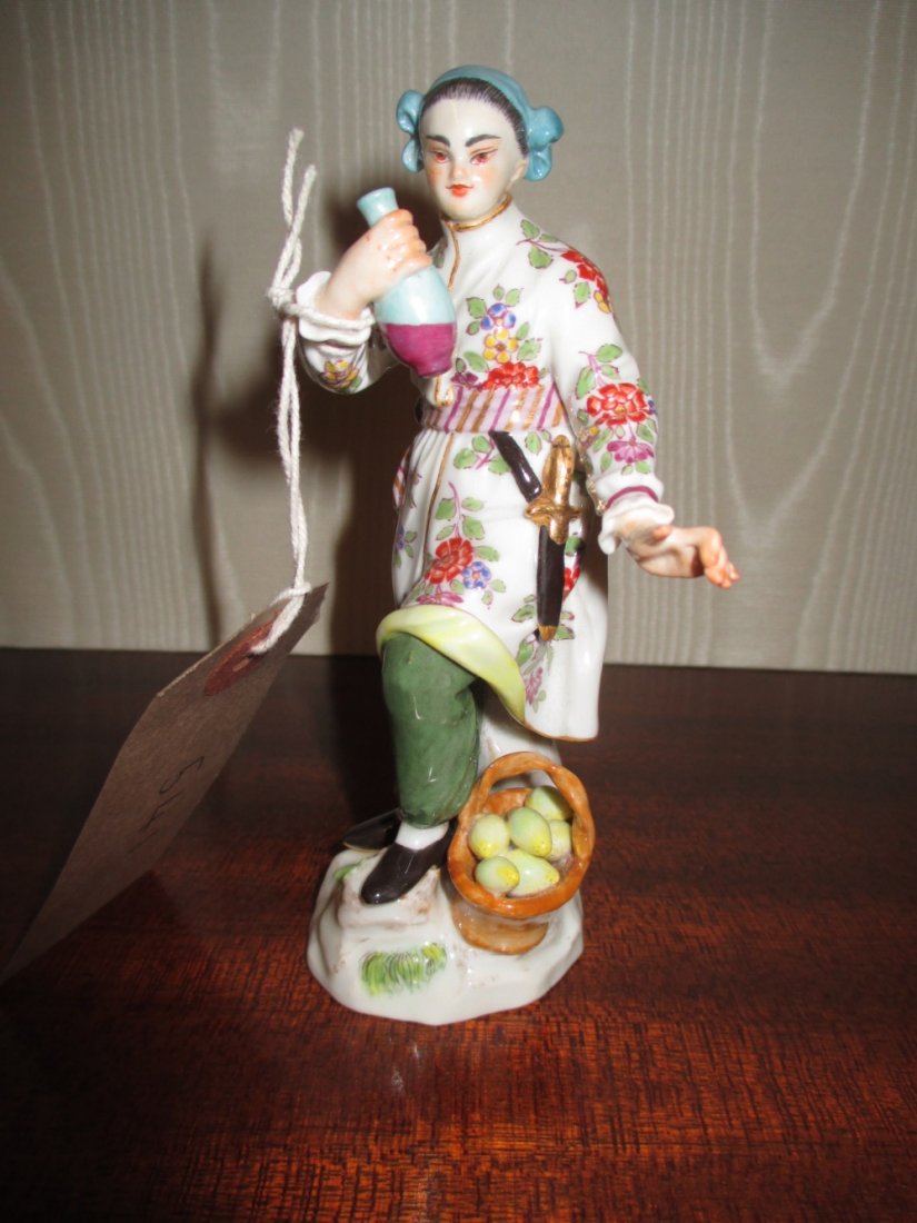 20th Century Meissen figure of a standing oriental girl: 20th Century Meissen figure of a standing oriental girl holding a flask of wine standing beside a basket of lemons, 4.75ins high