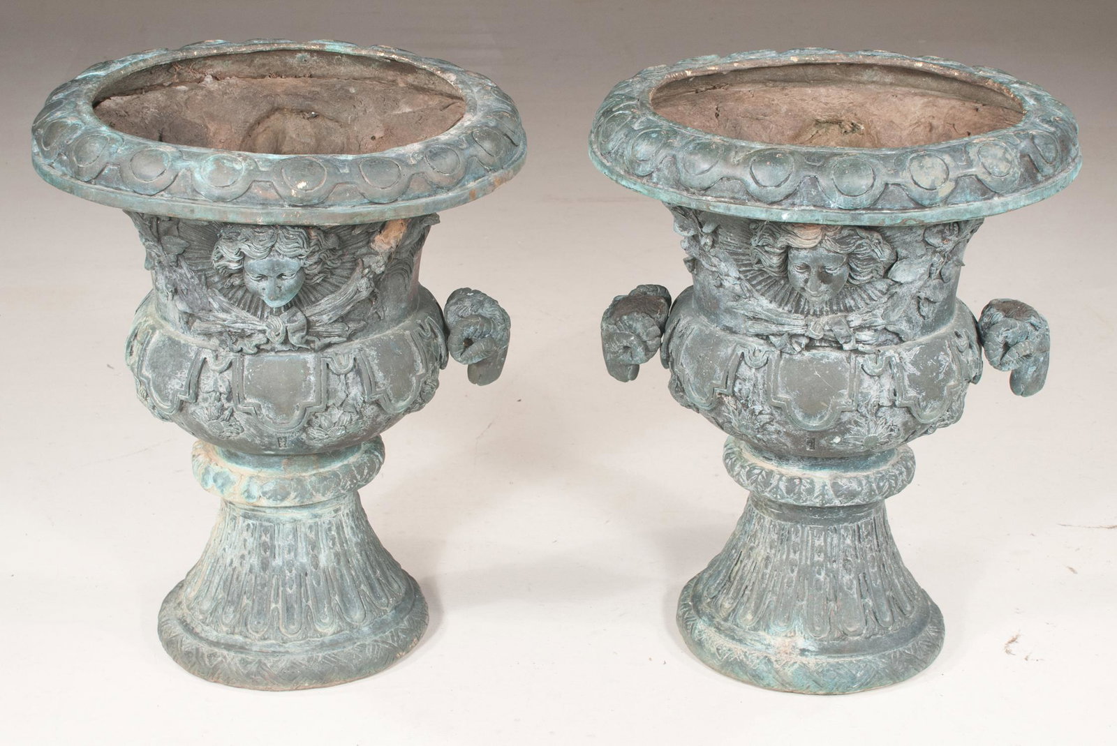 Pair of bronze planters with mask and swag decoration: Pair of bronze planters with mask and swag decoration having ram head handles and on fluted bases, 20" diameter, 25" high, one ram head is missing