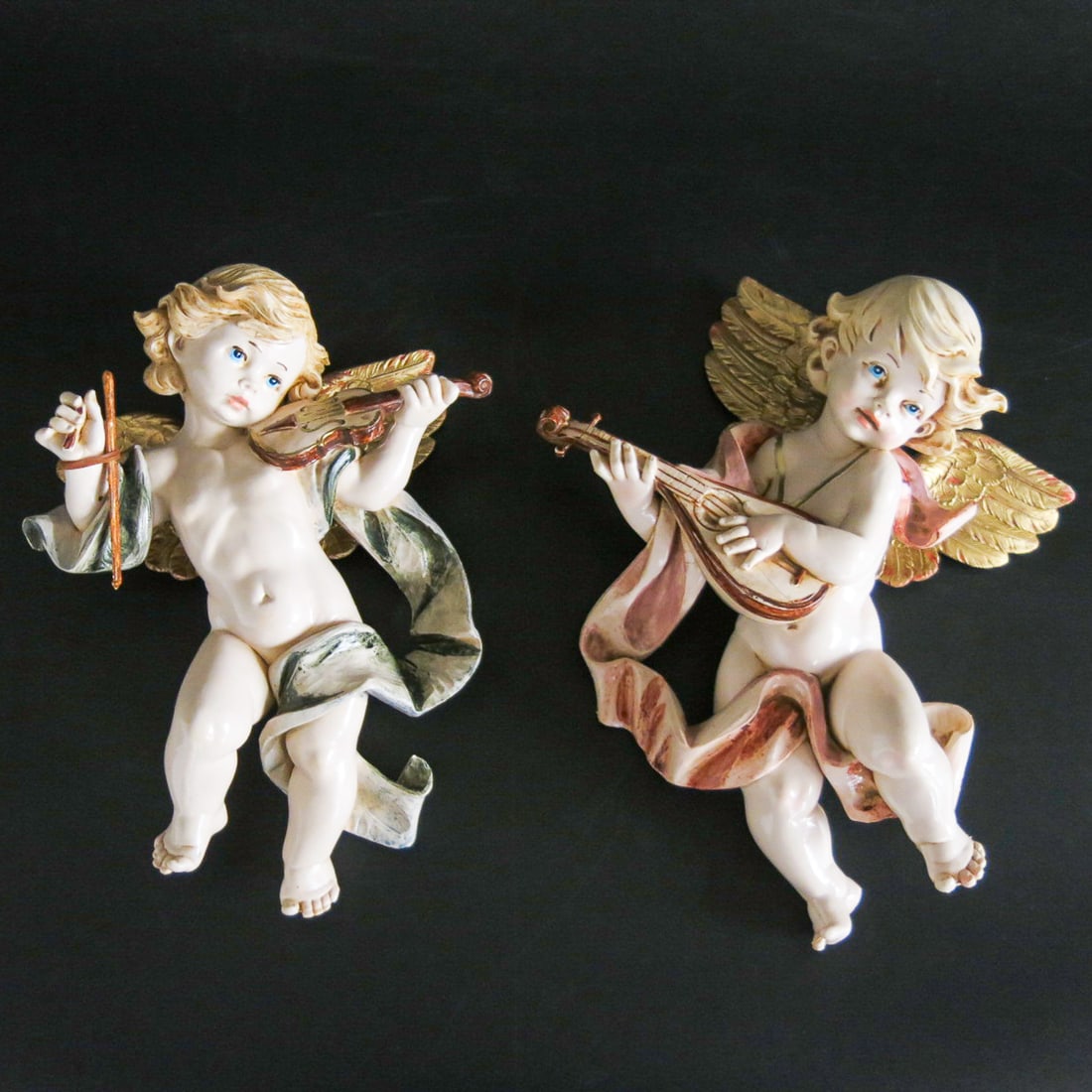 Italian Simonetti Composite Winged Putti Wall Mounts, Pair: Italian Simonetti Composite Winged Putti Wall Mounts, Pair, One Having Gold Wings, Pink Sash Covering and Playing Mandolin; The Other Having Gold Wings, Blue Sash Covering and Playing the Violin, Both