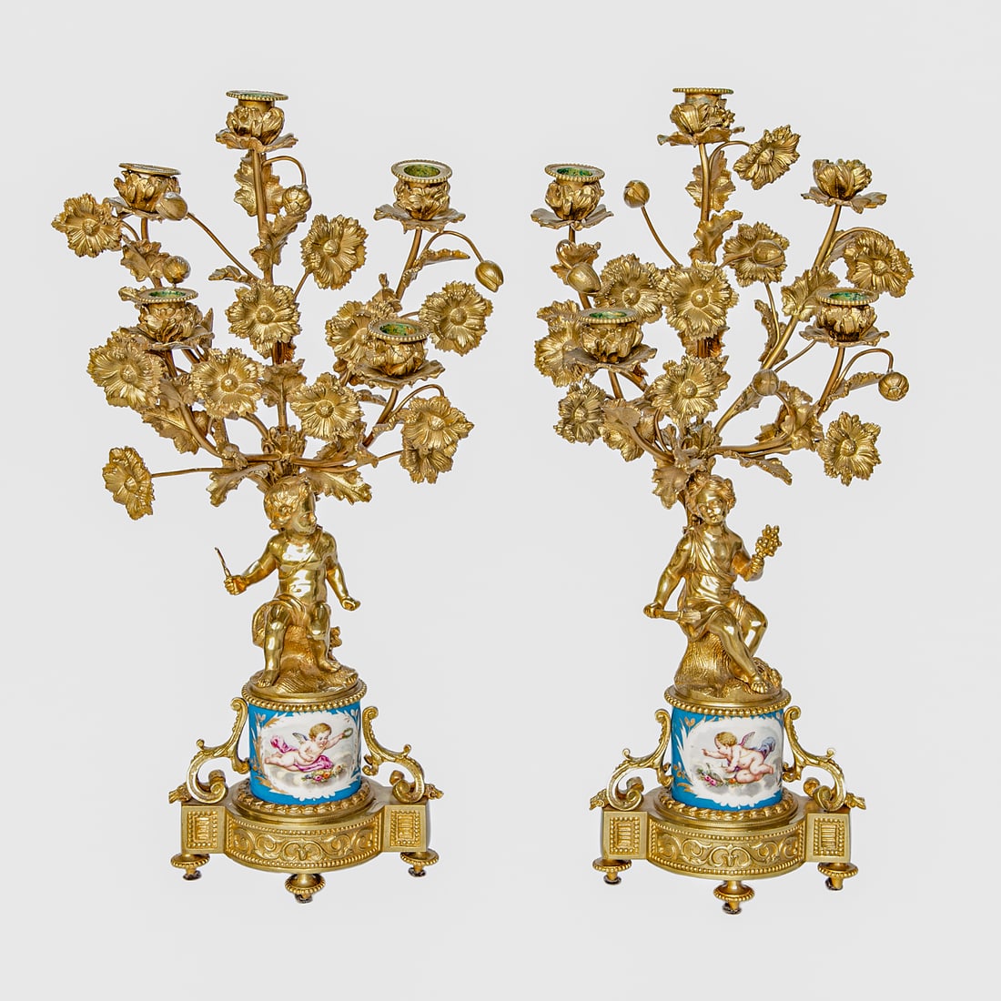 French Louis XV Style Gilt Bronze Five Branch Candelabra, Pair: French Louis XV Style Gilt Bronze Five Branch Candelabra, Pair, Having Five Cups Featuring Leaf Form Designs and Beaded Tops, Surrounded by Multiple Flowers and Buds, Atop Putti Figures, One Holding