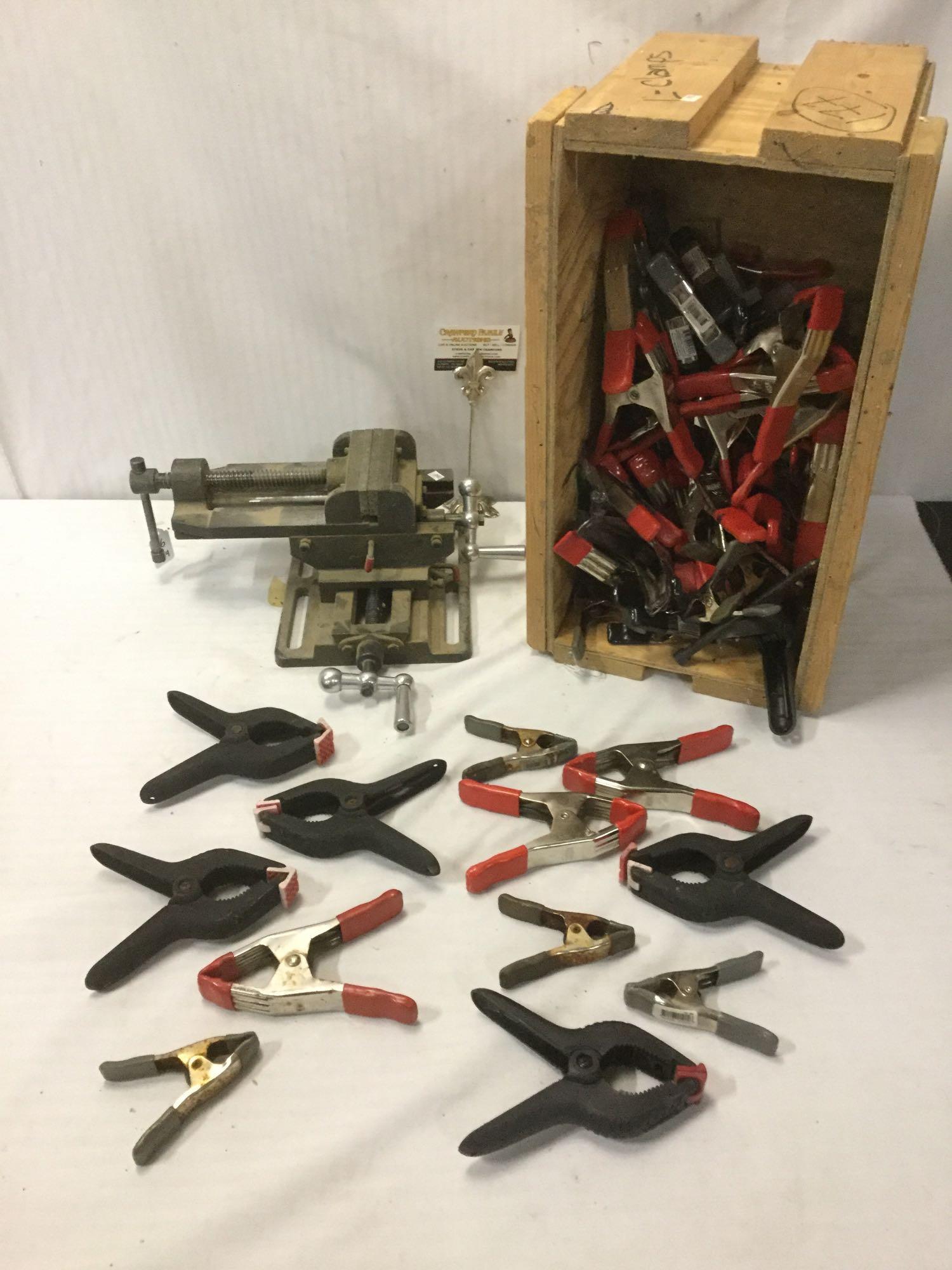 Mountable table vice clamp & small crate full of: Mountable table vice clamp & small crate full of approx. 25 clamps, clamps incl. brands like Stanley & Bessey, crate approx. 20x11x11 inches.