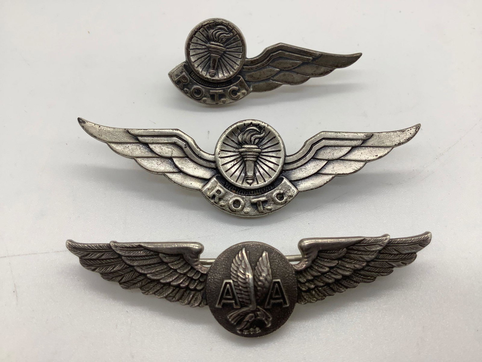 3 sterling silver aviation badges: ROTC Observer, ROTC: Collection of 3 sterling silver aviation badges. ROTC Observer, ROTC Pilot, and American Airlines crew pins. Ttw 32.7g. Largest approx 2.5x0.75x0.5 inches.