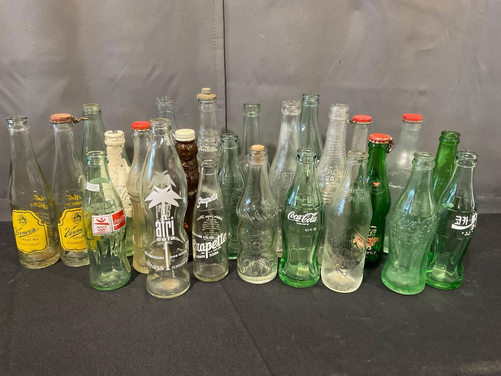 25 Glass Bottles, Afri-Cola, Coca-Cola incl 92 Barcelona Olympics, Vernor, Grapette & more: Appears to be in fair to good shape. Measures approx 14h x 14w x 13d inches. See pics. E-5360 *Oversized shipping may apply* 