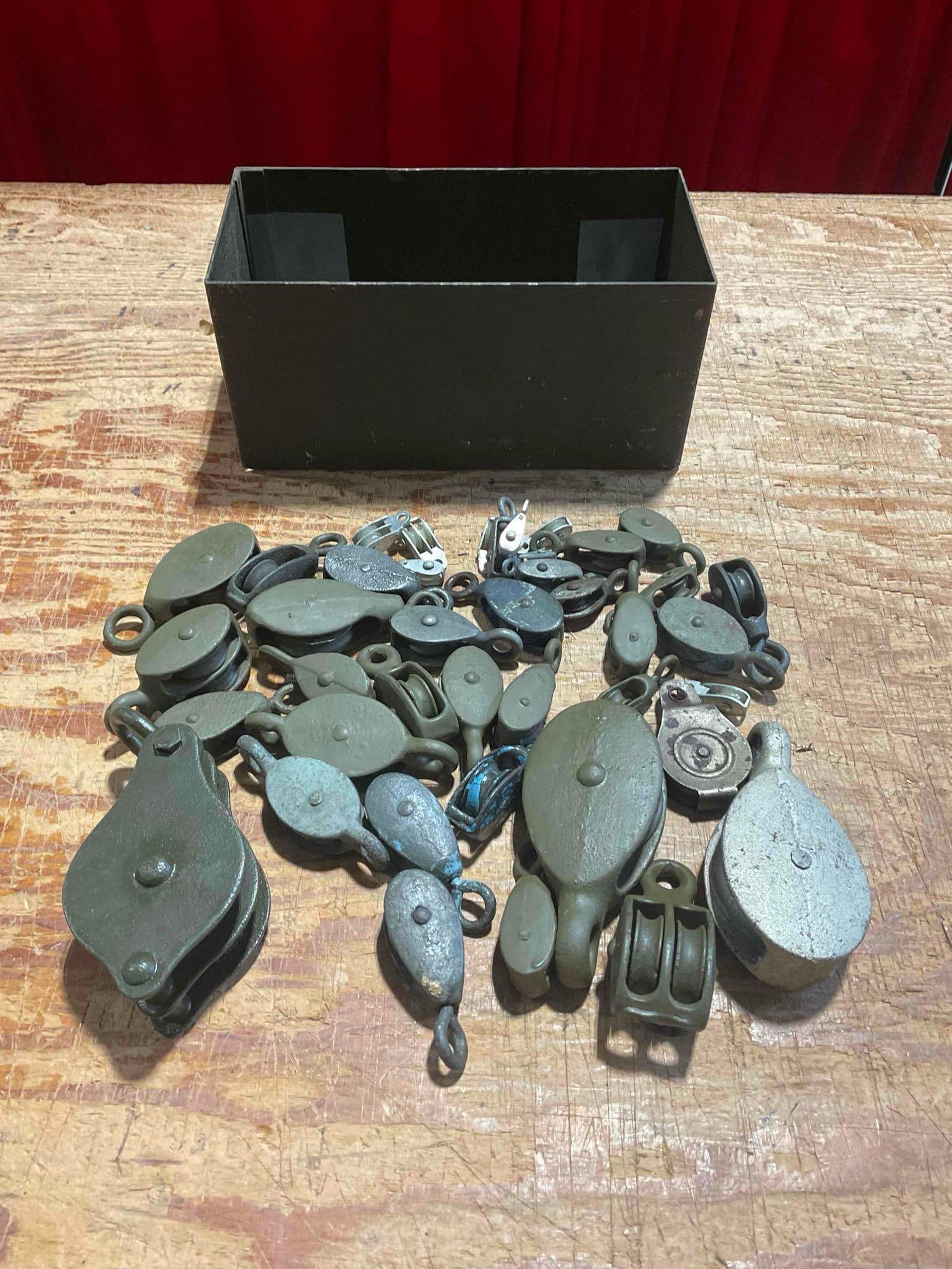 Collection of 30+ Small Cast Iron Pulleys and Metal Army Surplus Storage Bin: Approximately 10" x 6" x 6" items are in fair condition and all function. Largest pulley is 4" x 2" and has a double slot. V-5360 *Oversized shipping may apply* 