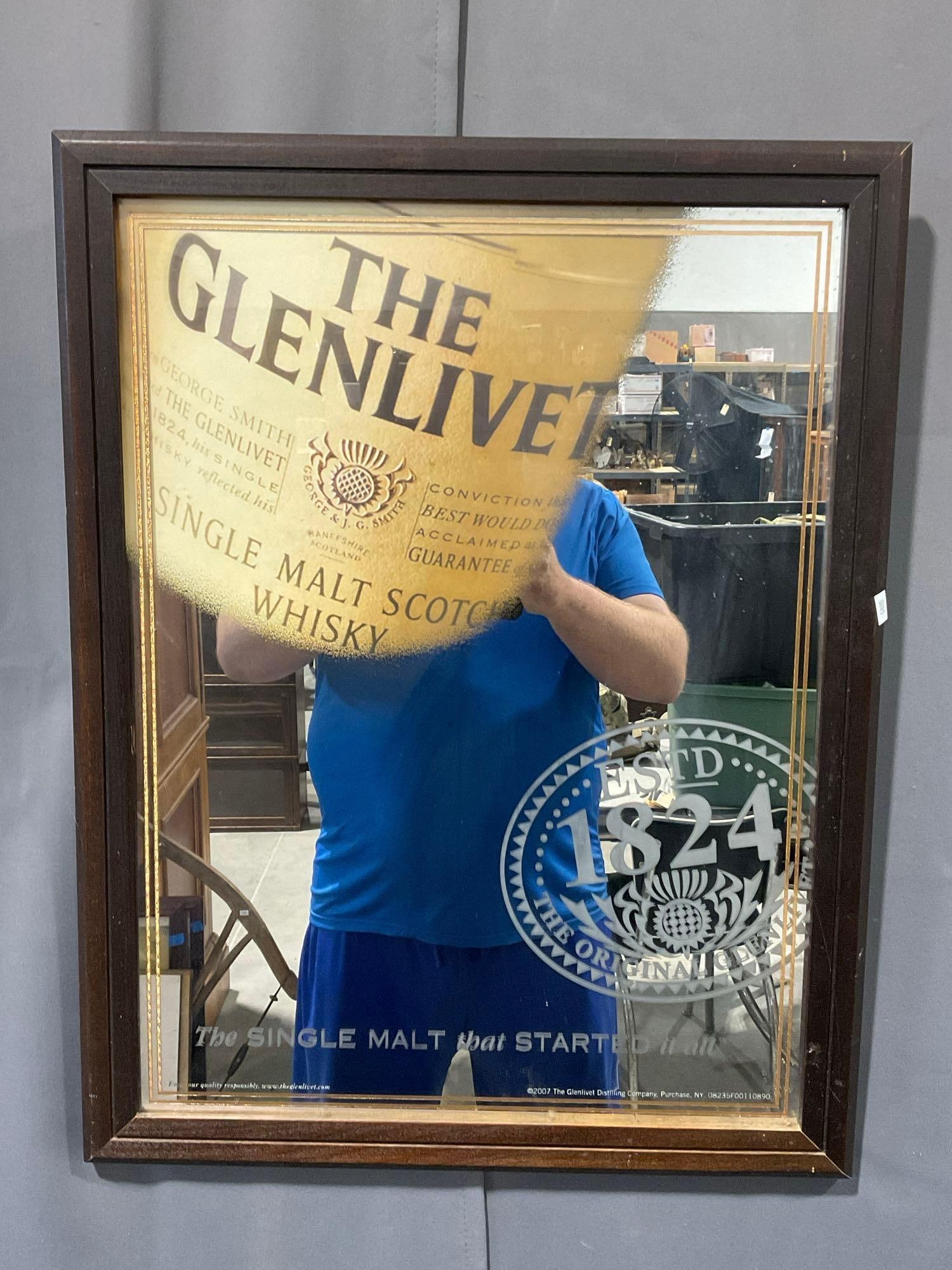 Framed 2007 Glenlivet Whisky Advertising Mirror, 28h x 22w inches, ESTD 1824: Sort of a cut out of the mirror to reveal the bottle design behind, Appears to be in fair to good shape, some wear on the frame. The piece measures approx 28h x 22w x 3d inches. See pics. E-5880
