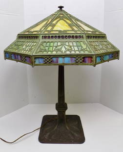 STAINED GLASS TABLE LAMP: A LARGE SLAG GLASS TABLE LAMP WITH DECORATIVE IRON BASE. FOUR DIFFERENT COLORS OF GLASS INCLUDES YELLOW ON TOP, A DEEP RED STRIP BELOW, A LARGE SECTION OF GREEN, AND THEN A MULTI COLORED BLUE AND RED