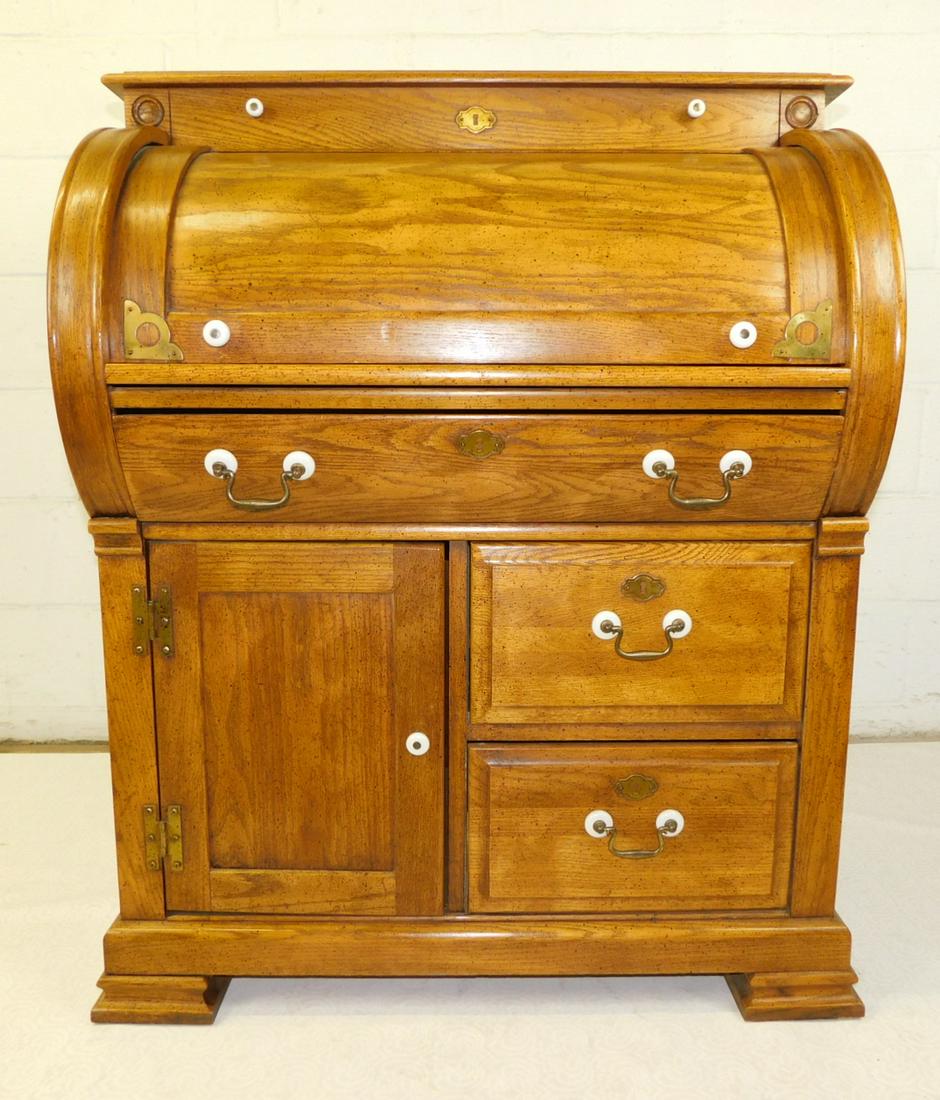 OAK CYLINDER DESK: AN OAK CYLINDER DESK WITH BRASS AND PORCELAIN HARDWARE. BY RIVERSIDE FURNITURE. MEASURES 32"W X 22"D X 42H.