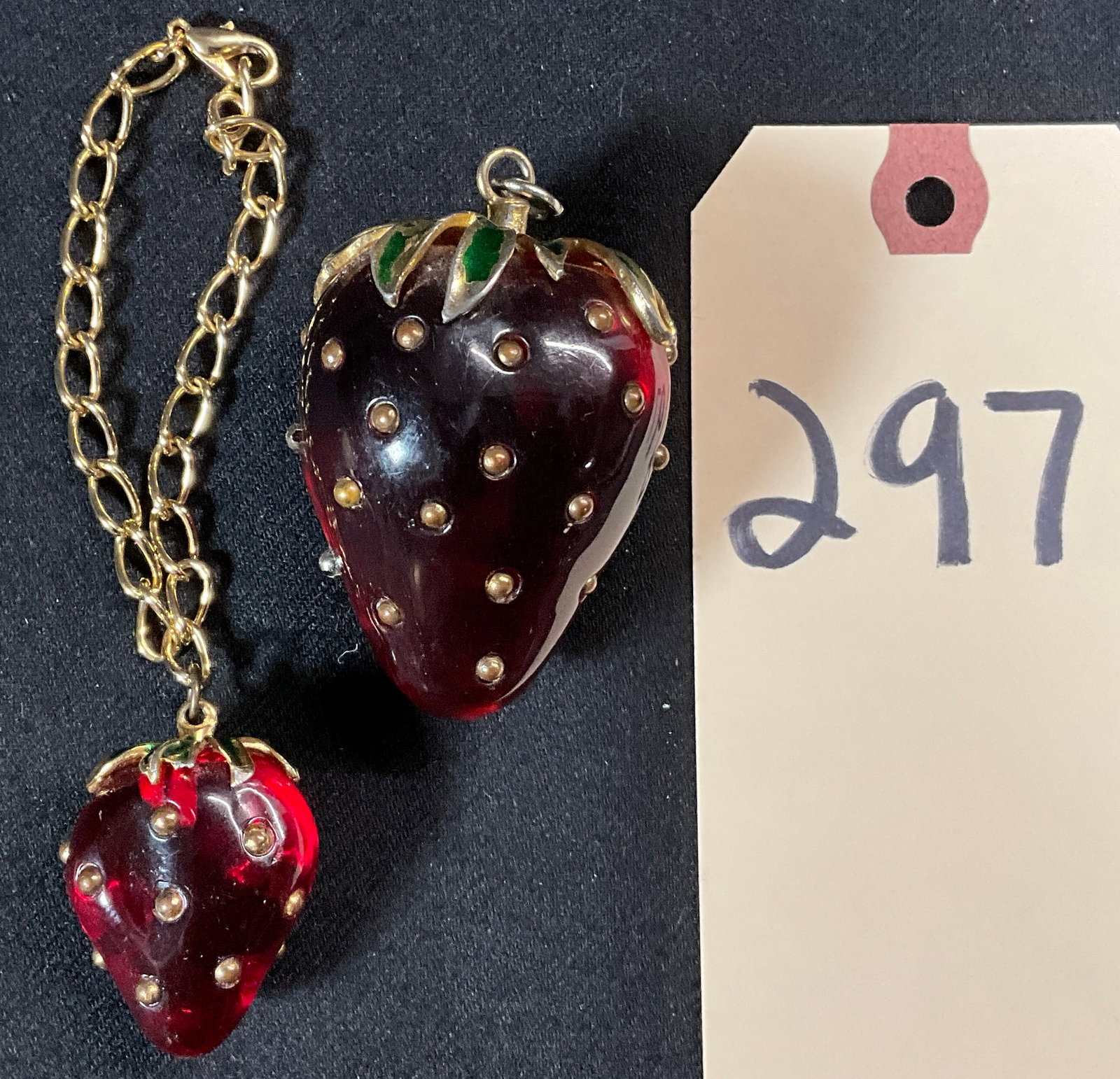 2 PC RED COMPOSITE STRAWBERRY PENDANT AND CHARM.: 2 PC RED COMPOSITE STRAWBERRY PENDANT AND CHARM. LARGE BERRY MEASURES 2" TALL, SMALL IS 1.5" TALL. Condition All property is sold in "as is" condition and all sales are final. Teel Auctions and its co