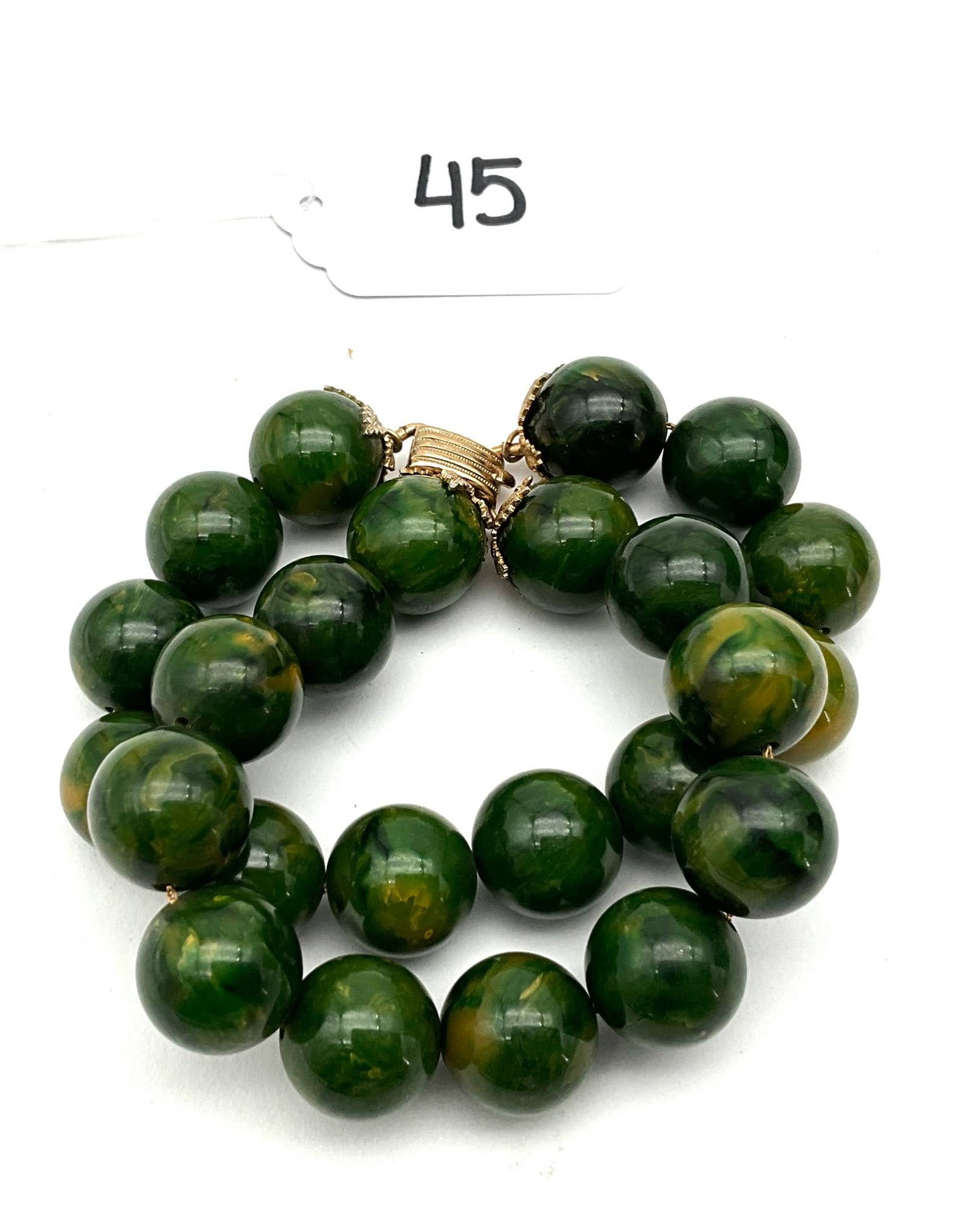 Bakelite Bracelet With Green and Yellow Marbled Beads, 8″L: Bakelite bracelet featuring green marbled beads with yellow accents, measuring 8 inches in length. The bracelet consists of two strands of spherical beads with a gold-tone clasp adorned with textured
