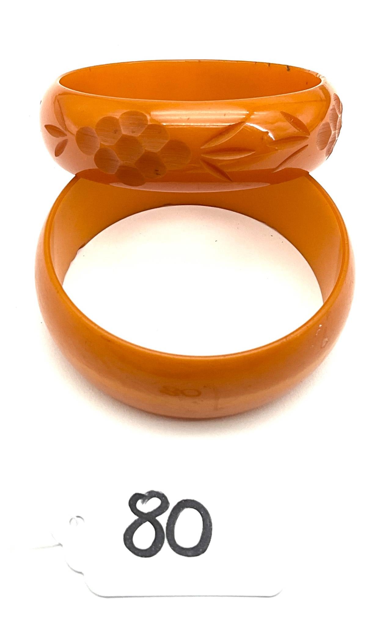 Carved Bakelite Bangles, .75″ to 1″ Wide x 2.5″ Diameter: Bakelite bangles featuring a carved design. One bangle is intricately carved with floral motifs, while the other is a smooth solid piece. Both measure approximately 0.75" to 1" wide with a 2.5" diamet