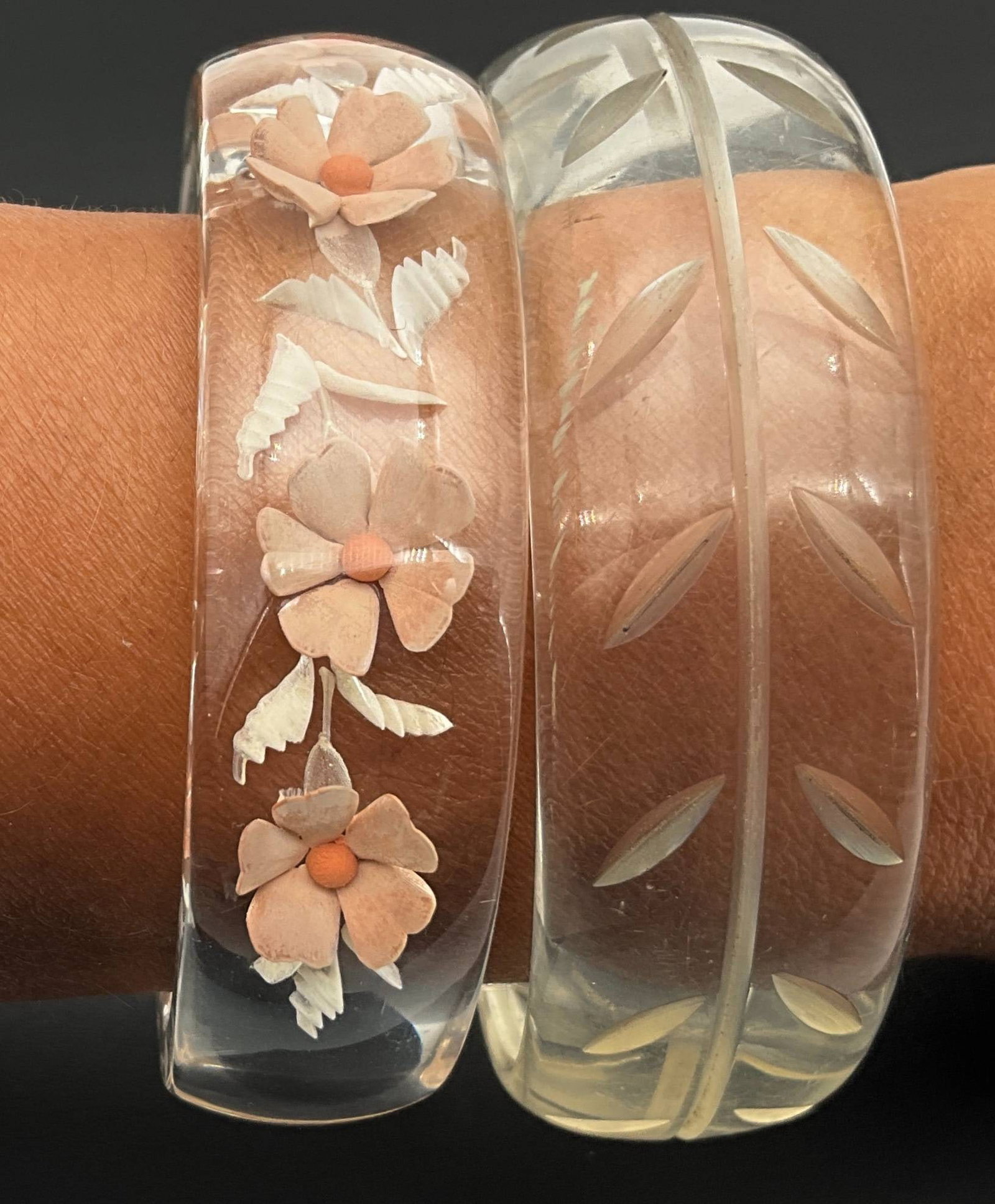 Lucite Bangles with Floral and Leaf Carvings: Lucite bangles featuring hand-carved designs. The first bangle measures approximately 0.75 inches by 2.25 inches in diameter and showcases engraved leaf patterns. The second, a semi-open design, measu