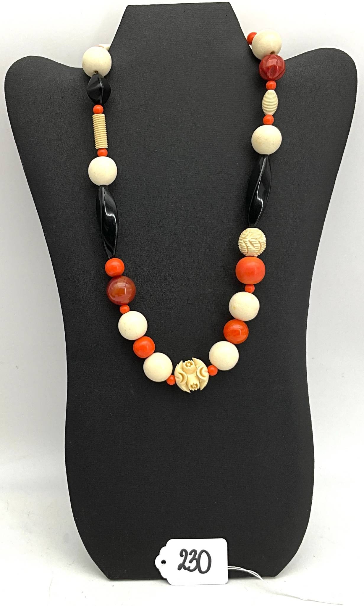 20-Inch Beaded Necklace with Mixed Materials Featuring Carved Centerpiece: 20-inch necklace featuring a variety of bead styles and colors, including cream, black, orange, and red beads. Notable elements include a carved centerpiece bead and accent beads of various shapes and