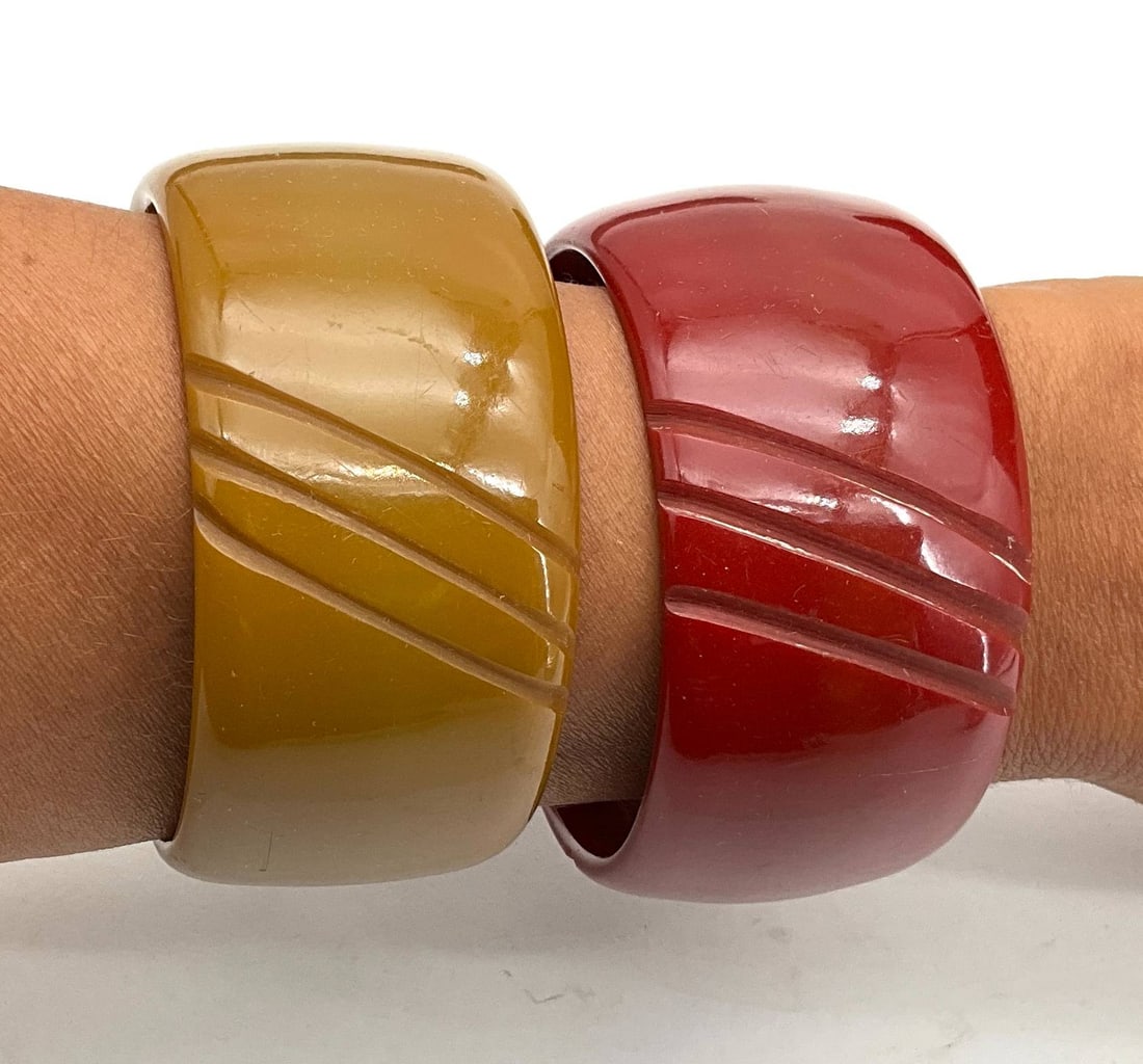 Carved Bakelite Bangles, Red and Mustard, 1.5 Inches Wide: Carved Bakelite bangles featuring vibrant red and mustard hues. Each bangle measures 1.5 inches wide with a 2.5-inch diameter. The geometric carved design lends a distinctive look, popular in mid-20th