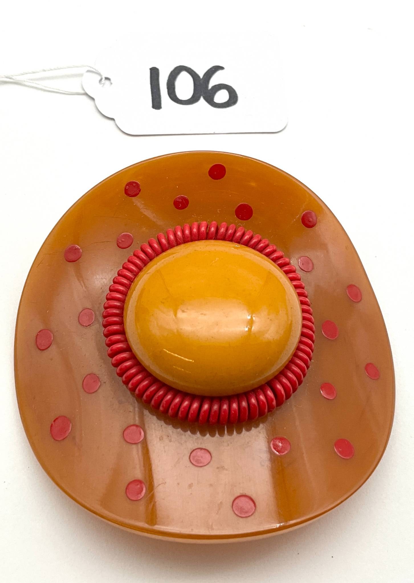 Vintage Bakelite Hat Motif Brooch, 3-Inch Diameter: This is a vintage brooch designed in a hat motif, crafted from bakelite. It measures 3 inches in diameter. The piece showcases a central yellow dome surrounded by a red coiled design and red polka dot