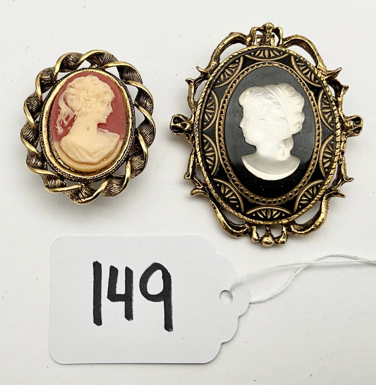 Victorian Gold-Tone Cameo Brooch Pair with Larger Brooch: Victorian-style cameo brooches featuring intricately detailed gold-tone frames. The larger brooch measures 1.75 inches wide by 2 inches tall and displays a black and white cameo motif. The smaller bro