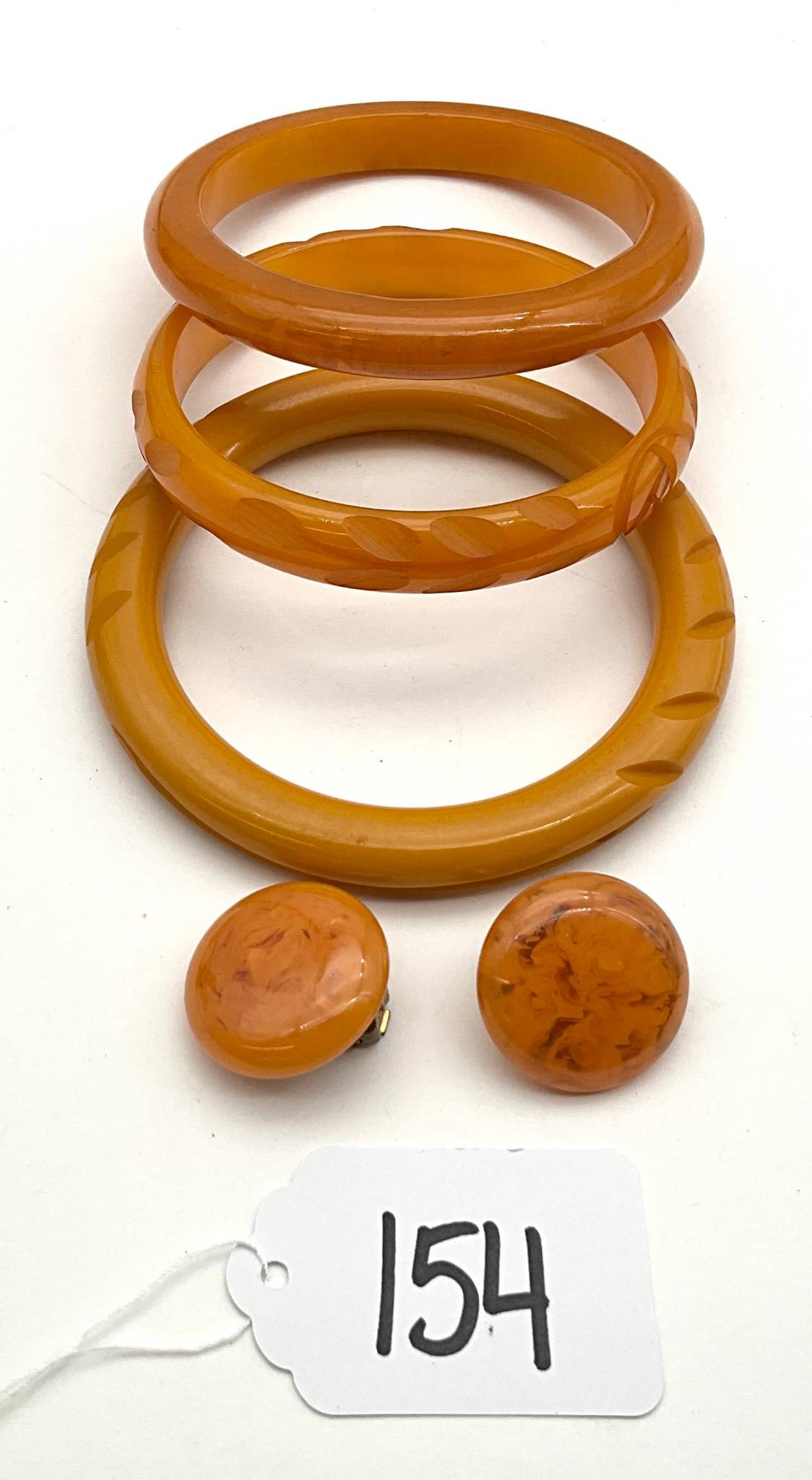 Vintage Bakelite Bangles and Clip-On Earrings Set: Three vintage Bakelite bangles and a pair of Bakelite clip-on earrings. The bangles feature unique carved patterns with a warm yellow-orange tone. The clip-on earrings showcase a marbled design in sim