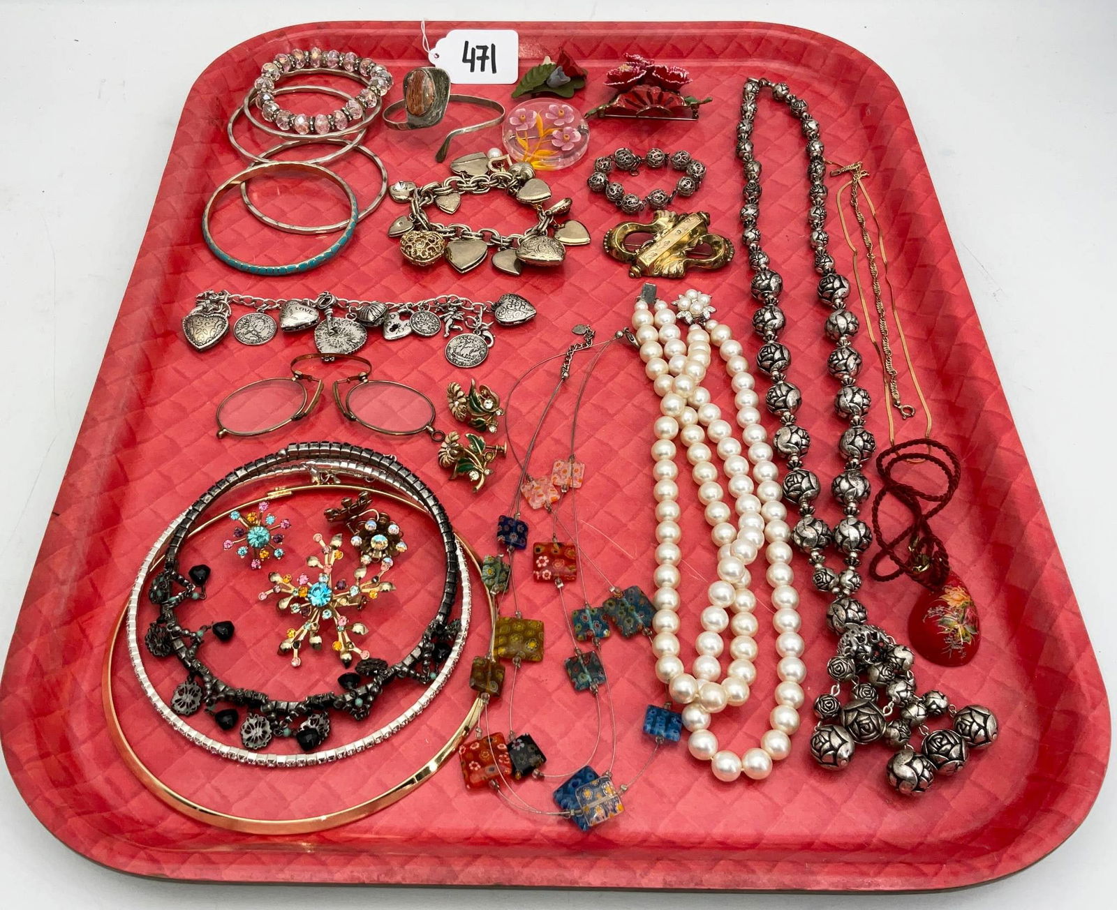 Costume Jewelry Including Bangles, Necklaces, and Brooches: A varied collection of costume jewelry displayed on a red tray, including multiple bangles, necklaces, brooches, earrings, bracelets, and pendants. Highlights include a chain-link bracelet with heart