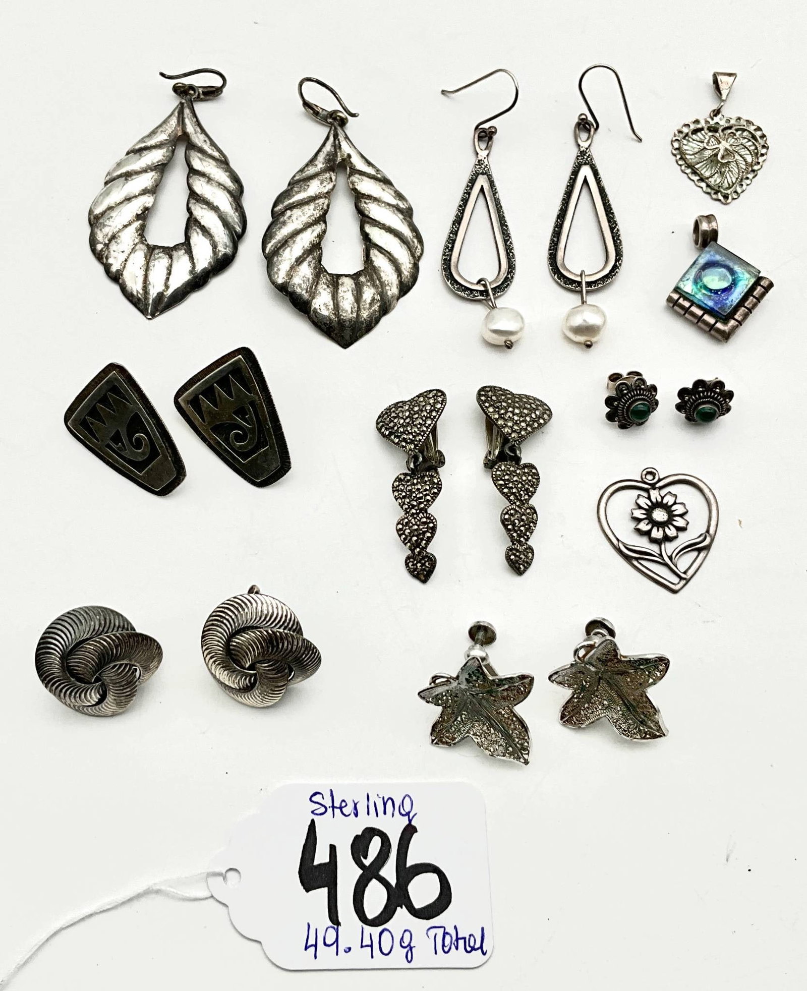 Sterling Silver Jewelry Including Earrings and Pendants, 49.40 Grams Total: Sterling silver jewelry weighing a total of 49.40 grams. Includes an assortment of earrings (some paired with pearls), decorative pendants, and other pieces featuring diverse designs such as hearts, f