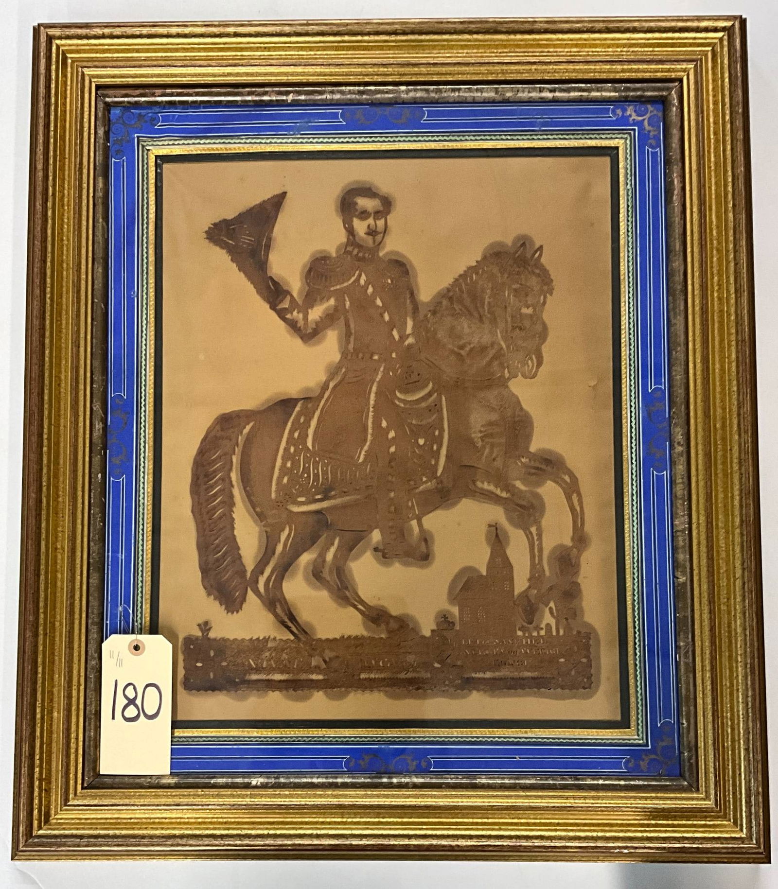 Vintage Equestrian Scherenschnitte in Decorative Frame, 25 x 29 Inches: Scherenschnitte paper art depicting an equestrian rider in detailed attire on horseback, mounted against a scenic background with buildings and foliage. Presented in a vintage wooden frame with blue-p