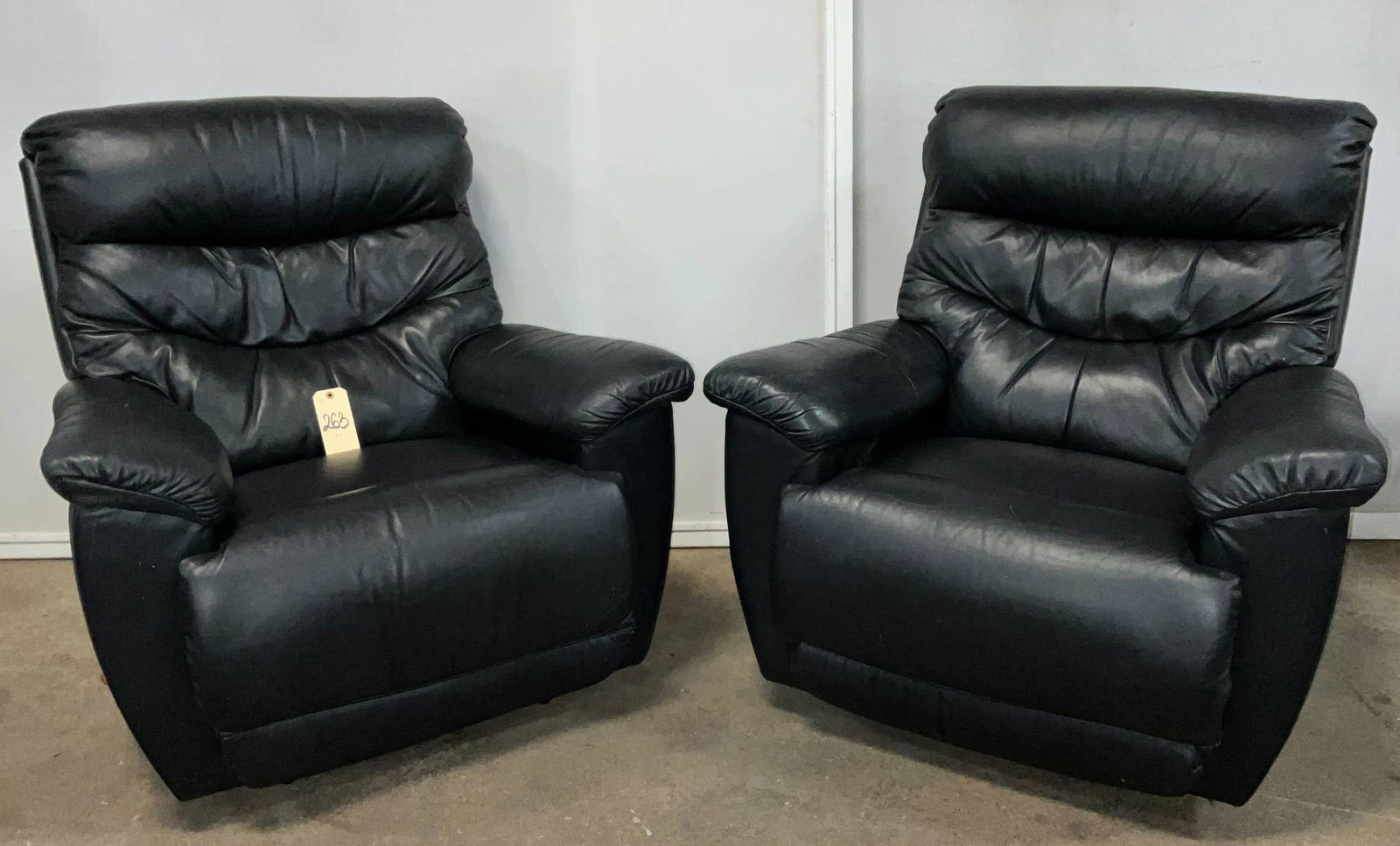 Lazy Boy Black Leather Recliners with Manual Reclining Mechanism: Two La Z Boy recliners upholstered in black leather. Each recliner measures approximately 39 inches wide, 40 inches high, and 20 inches high from floor to seat. Features include padded armrests, a hig