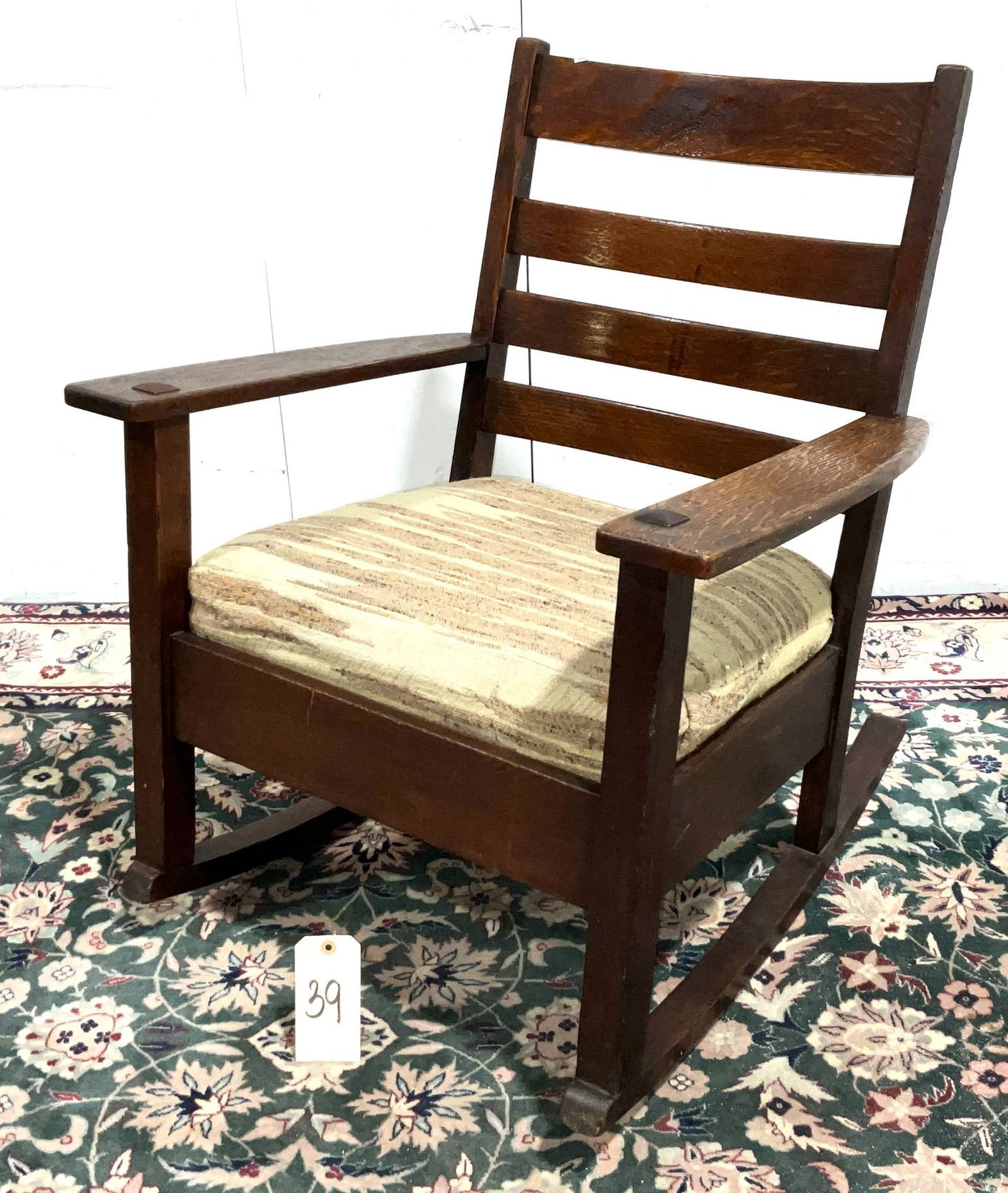 Early 20th Century Oak Ladder-Back Rocking Chair with Upholstered Seat: An early 20th century oak rocking chair featuring a ladder-back design with horizontal slats. It includes a cushioned seat upholstered with striped fabric. The chair measures 27 inches wide by 28 inch