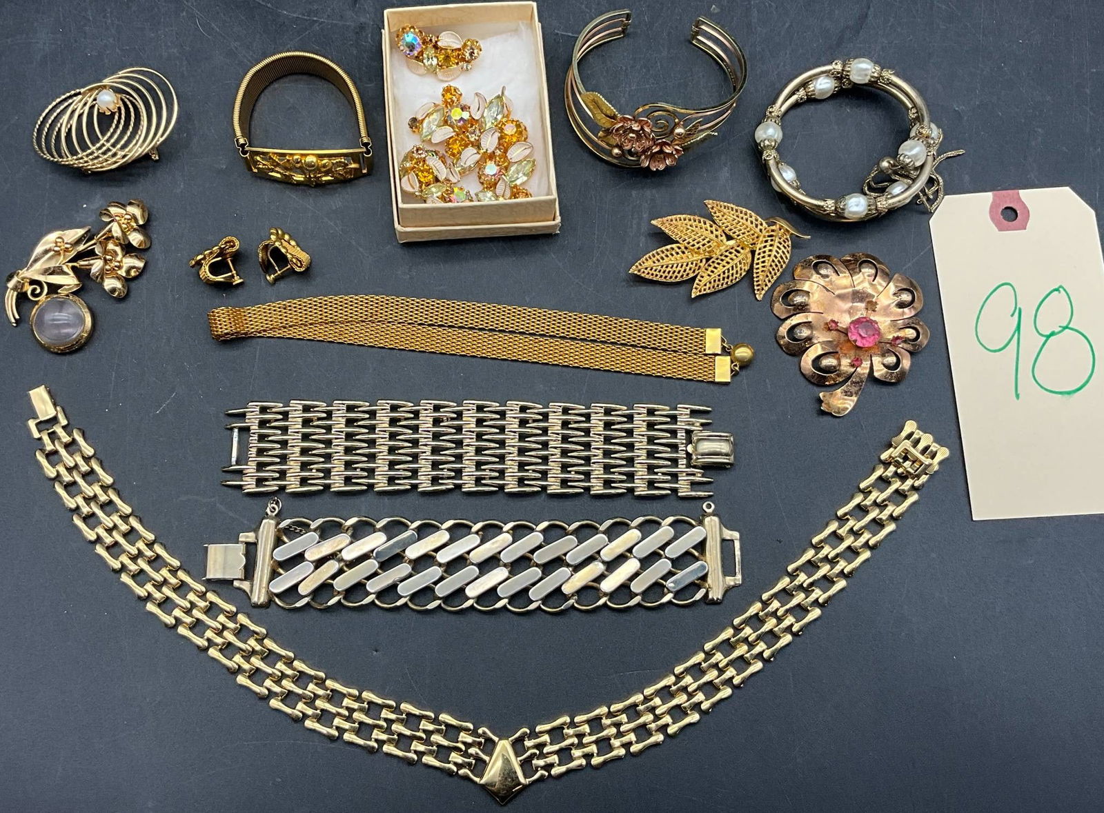 Gold-Toned Jewelry Including Coro, Austria, and Others: Gold-toned jewelry including bracelets, brooches, earrings, and a necklace. Highlights include a floral brooch with pink rhinestone accent, a leaf motif brooch, multiple chain-link bracelets, and a pa